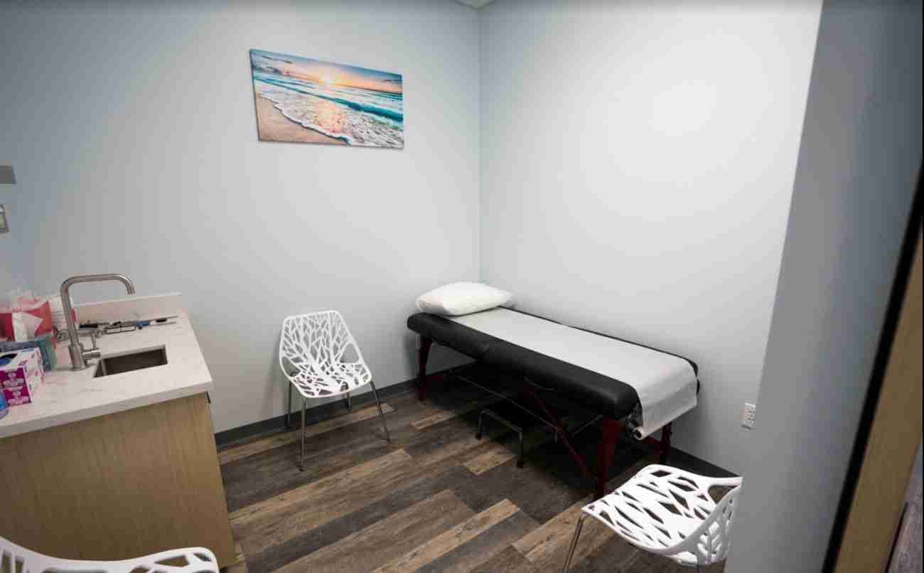 Exam room at Dr. Paul Morton's orthopedic clinic with a treatment table, modern chairs, and ocean artwork on the wall.