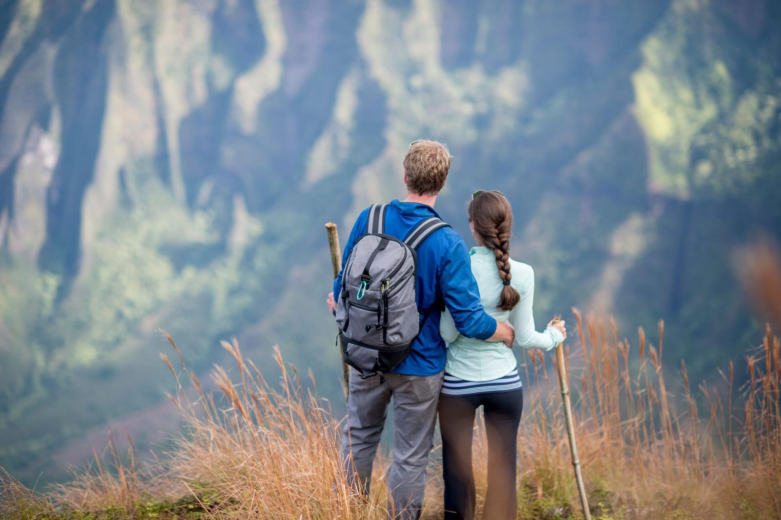 A couple pauses on a grassy ridge to take in the view of Hawaii's fluted green cliffs while hiking.