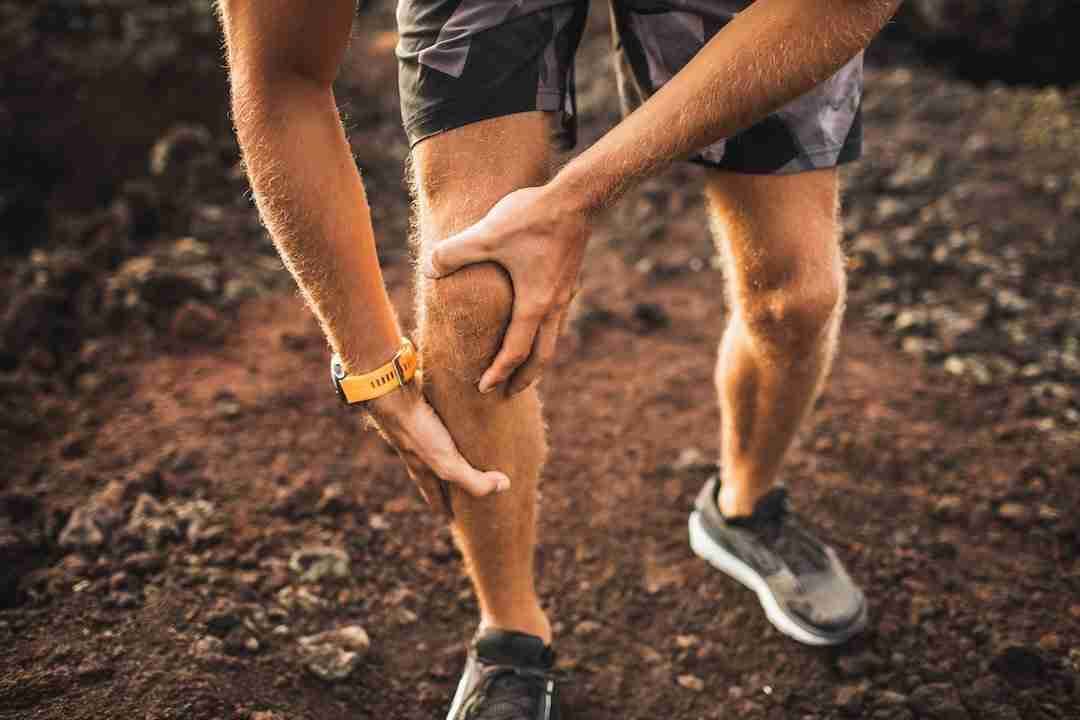 A trail runner grips his knee in pain on a red-dirt Hawai‘i path, illustrating knee pain during activity.