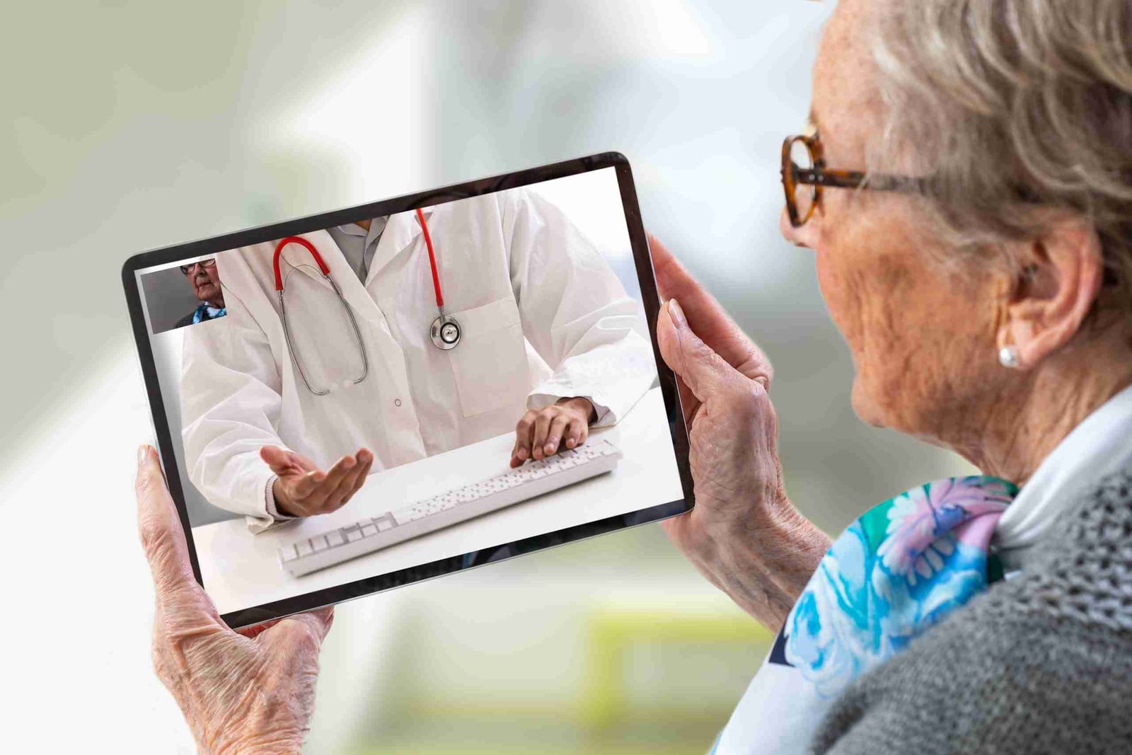 An older woman holds a tablet during a telehealth video visit with a doctor.