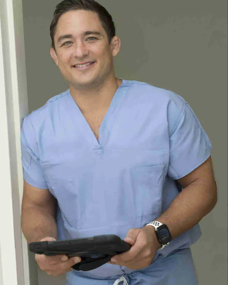 Dr. Paul Morton, hip and knee replacement surgeon in Honolulu, smiling in light blue scrubs while holding a tablet.