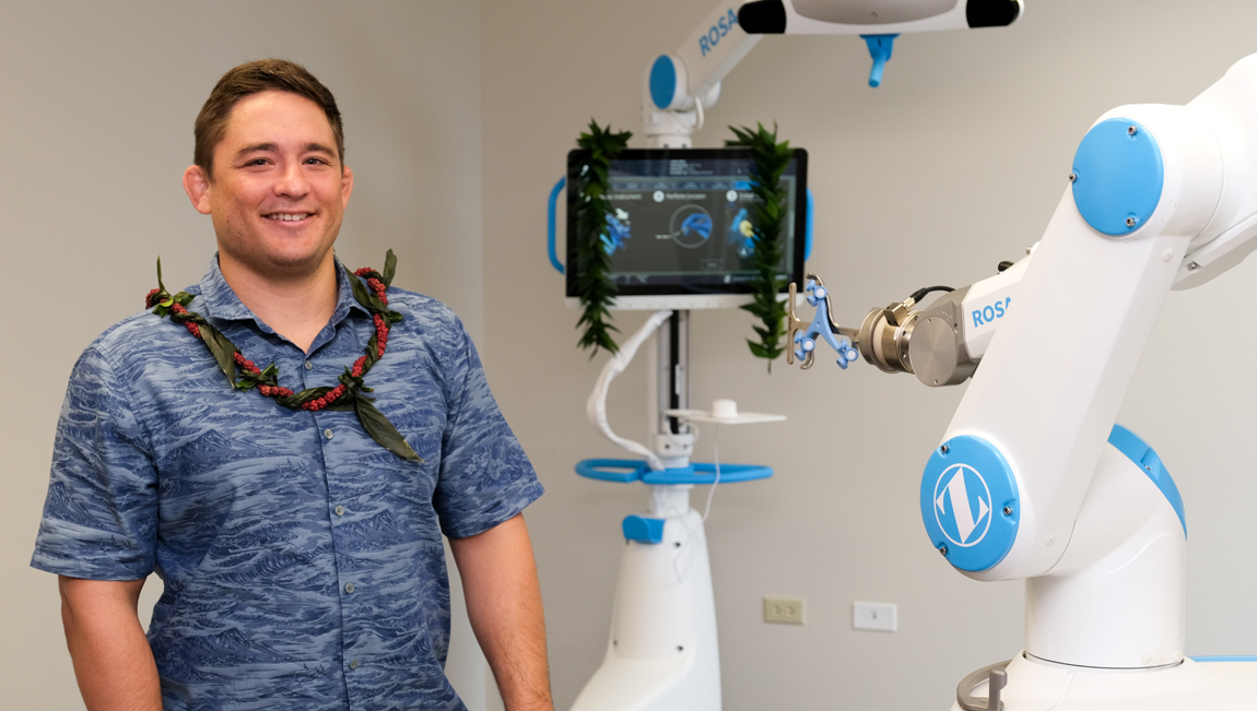 Dr. Paul Morton wearing a maile lei beside the ROSA Knee robotic surgery system in Honolulu.